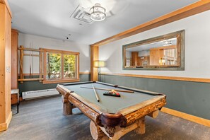Une table de billard avec des billes, un miroir et une fenêtre donnant sur des arbres.