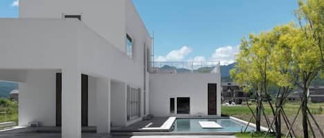 A modern building with a pool, outdoor seating, and a clear sky.