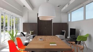 A modern meeting room with a wooden table, colorful chairs, a large white pendant light, and a view of the outdoors through large windows. - Water House (Yilan)