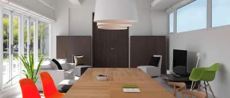 Un espace de salle à manger moderne avec une table en bois, plusieurs chaises, un grand luminaire suspendu et une vue dégagée grâce à de grandes fenêtres.