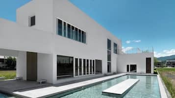 Uma casa moderna de dois andares com piscina, janelas amplas e telhado plano.