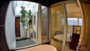 A modern bathroom with a glass-enclosed shower, a large bathtub, and a view of a bedroom with a bed and a nightstand. - Water House (Yilan)