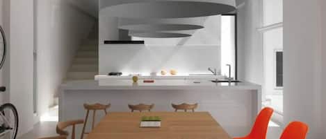 A modern kitchen with a built-in island, a dining area with a wooden table and orange chairs, and a staircase leading to an upper level.