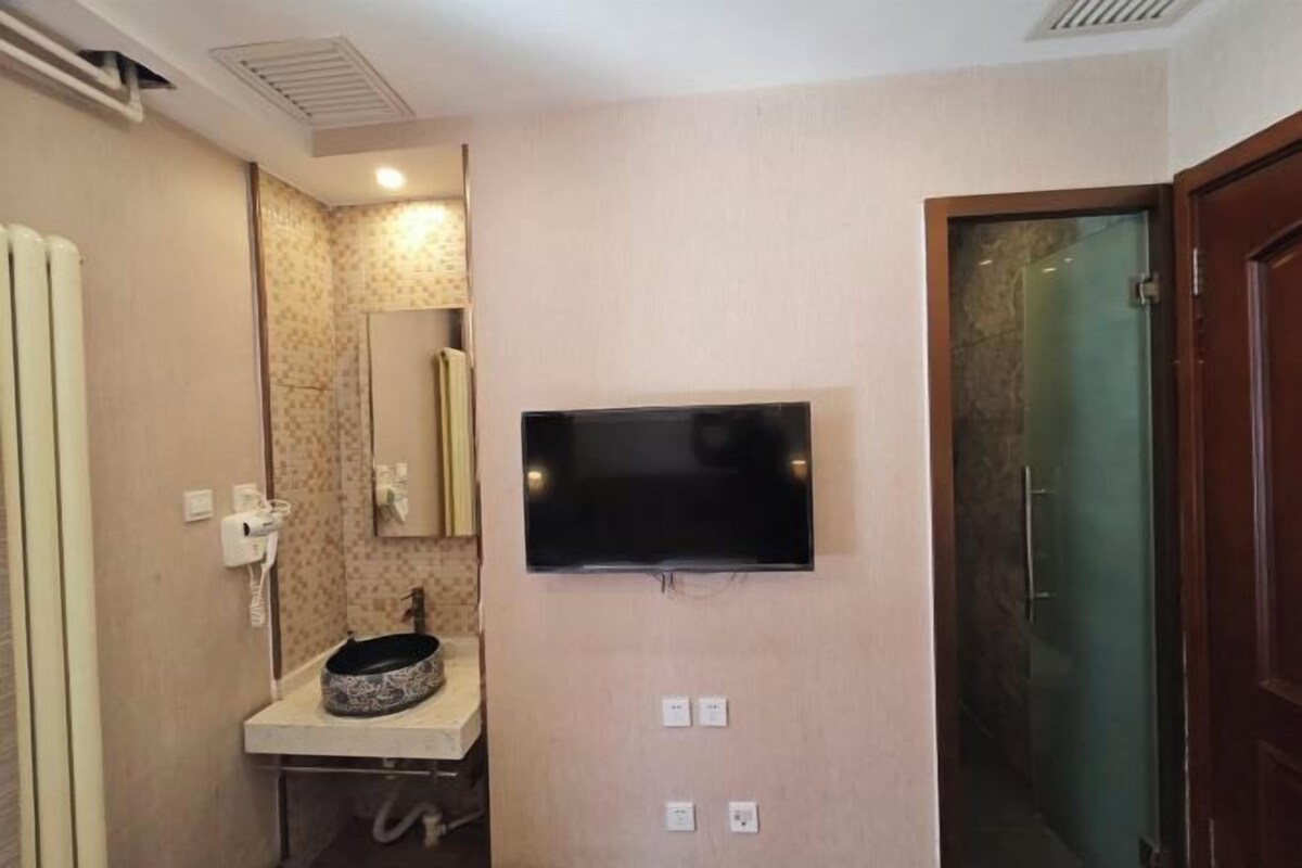 Un baño con lavamanos, espejo y un televisor fijado a la pared.
