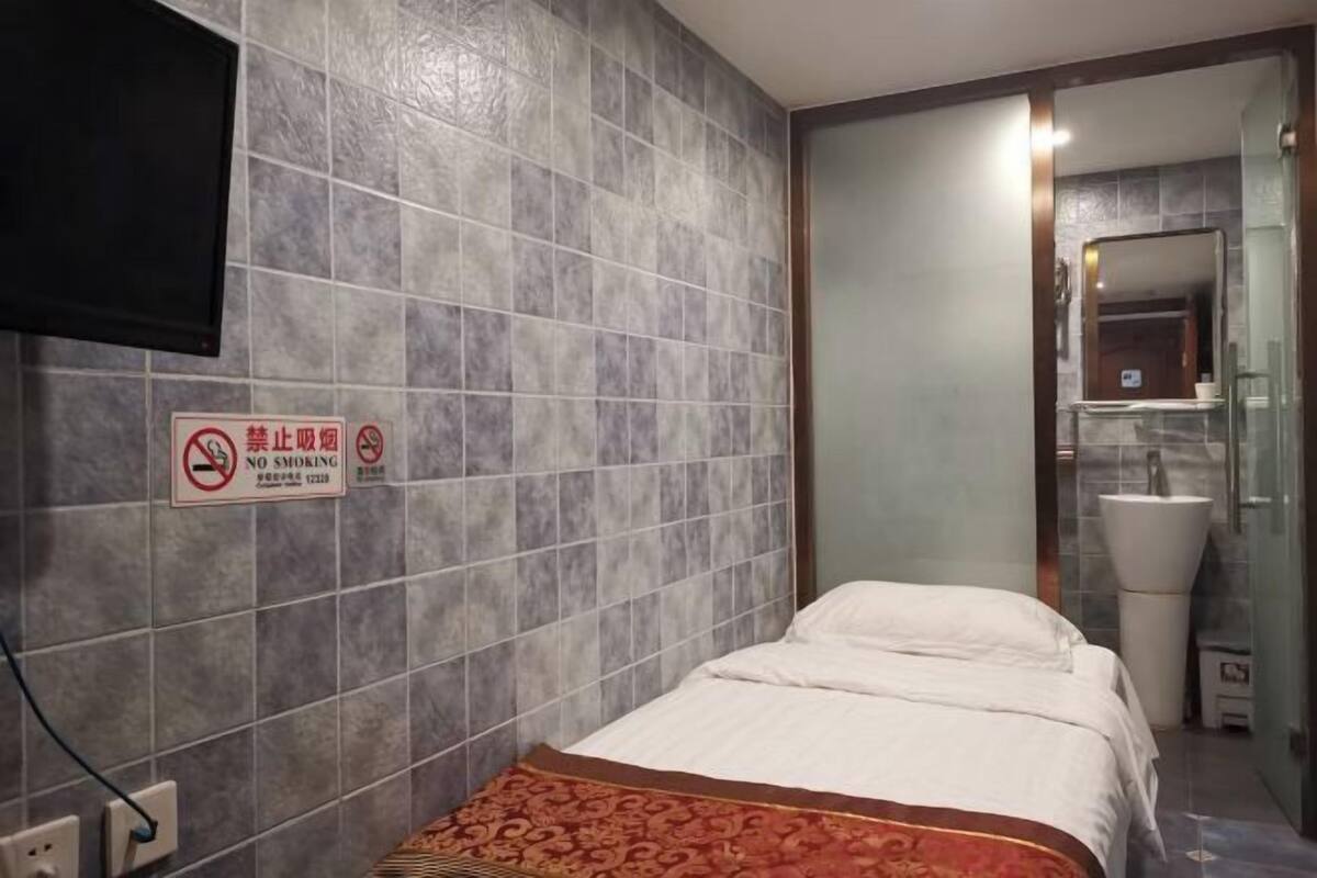 A hotel room with a bed, a no-smoking sign, a television, and a bathroom with a sink and mirror.