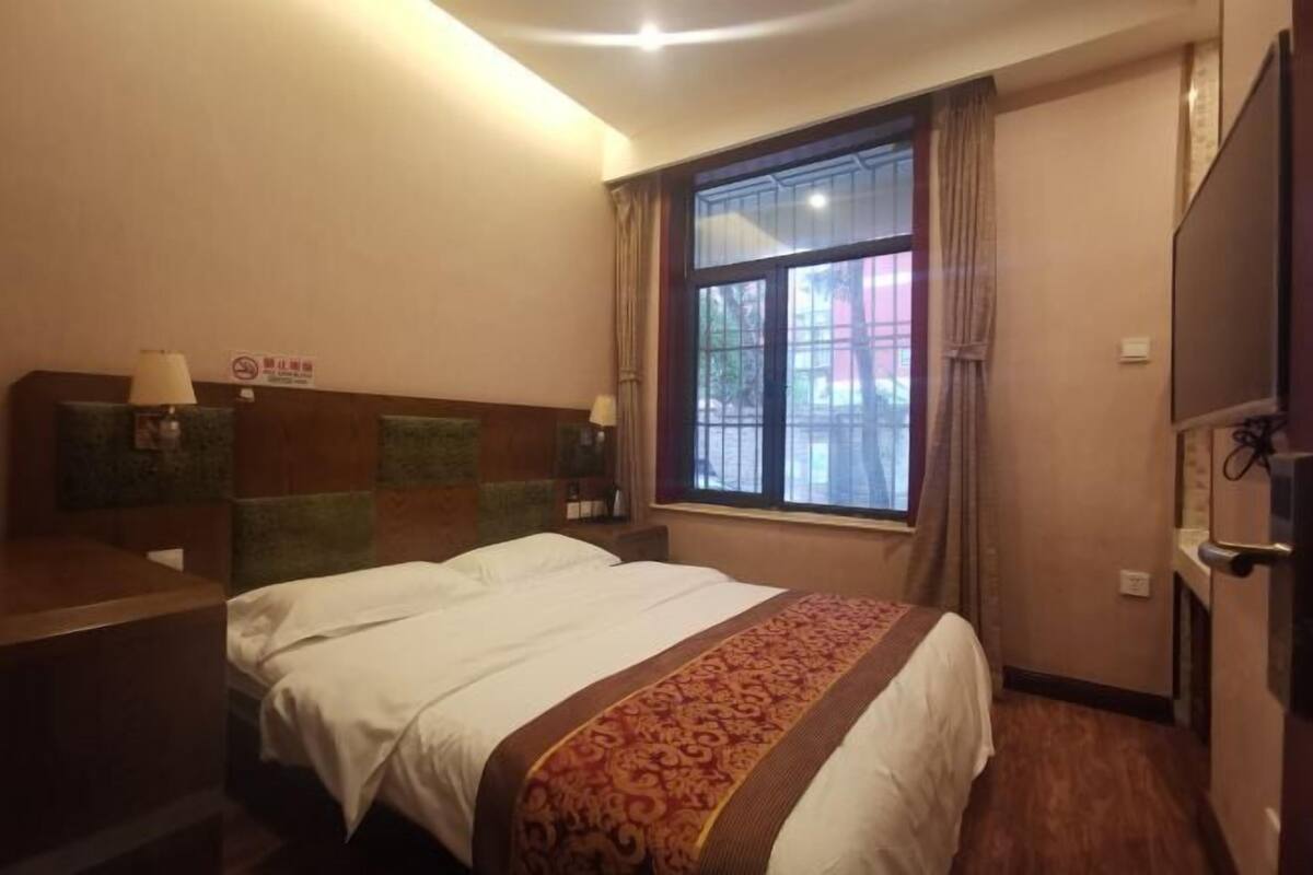 A hotel room with a bed, a desk, a window with curtains, and a television.
