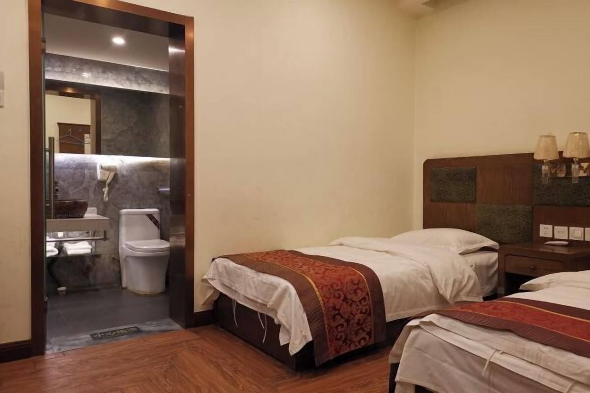 A hotel room with two beds, a wooden floor, a bathroom with a toilet and sink, and a nightstand with lamps.