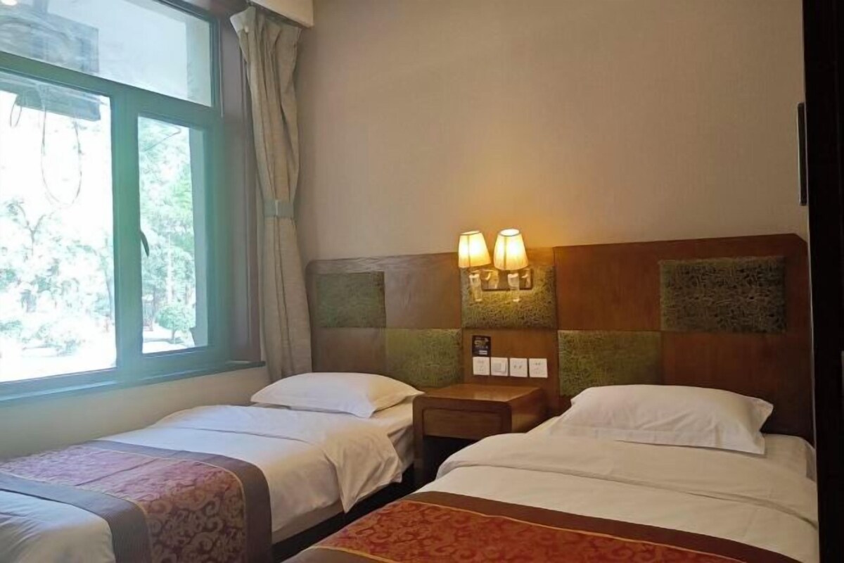 Una habitación de hotel con dos camas individuales, una mesita de noche con lámpara y una ventana con cortinas.