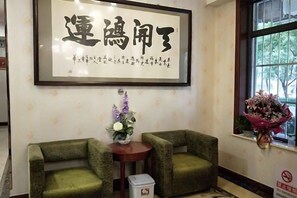 A room with two green chairs, a small table with a vase of flowers, and a framed calligraphy piece on the wall. - Beijing Tiantan Huiqingyuan Hotel (Beijing)