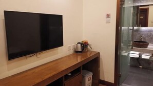 A room with a flat-screen TV mounted on the wall, a wooden console table, a trash bin, and a glass shower enclosure. - Beijing Tiantan Huiqingyuan Hotel (Beijing)