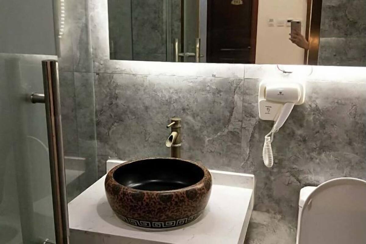 A bathroom with a round vessel sink, a handheld showerhead, a towel rack, and a mirror.