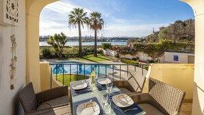 Ein Balkon mit Tisch für zwei Personen, Blick auf einen Pool und eine Stadtlandschaft mit Palmen.