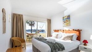 Ein Hotelzimmer mit einem Bett, einem Holzstuhl, einem kleinen Tisch und Blick auf eine Stadtlandschaft durch ein großes Fenster.