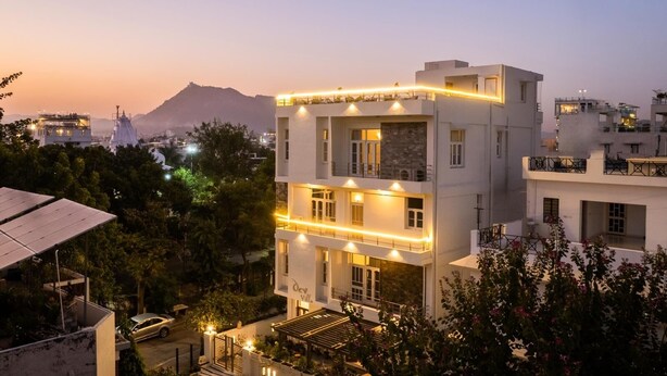 Un immeuble à plusieurs étages doté de balcons, une enseigne indiquant « Doc Villa », et un paysage montagneux en arrière-plan.
