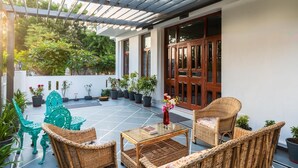 Une terrasse couverte, aménagée avec des meubles en osier, des plantes en pot et une porte en bois.