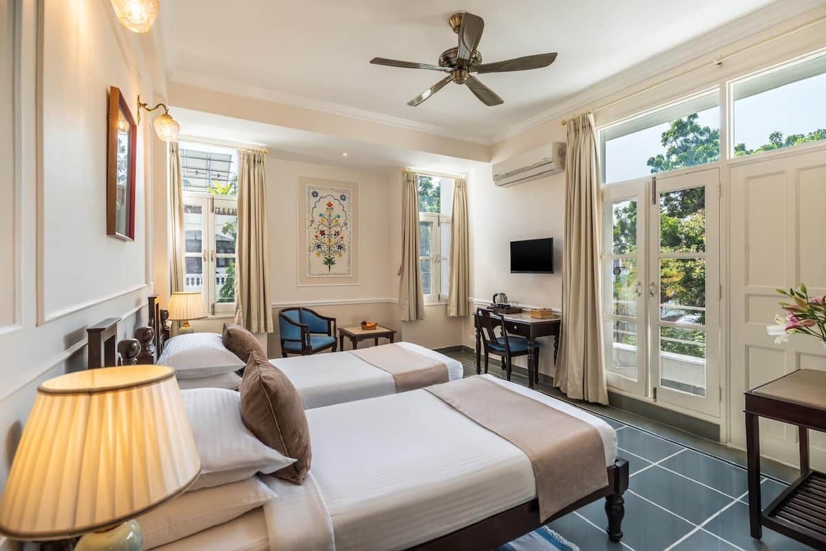 A hotel room with two beds, a desk, a chair, a television, and large windows.
