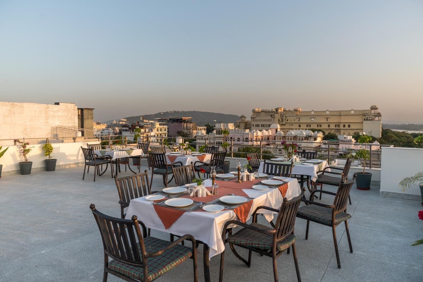 Un espace de restauration aménagé sur le toit, avec des tables pour deux, entouré de plantes en pot et offrant une vue sur le paysage urbain.