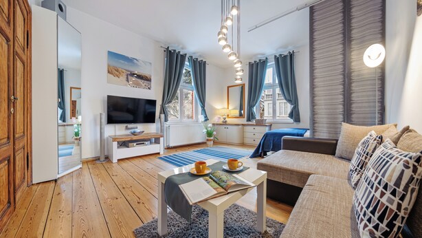 A modern living room with a TV, wooden flooring, a sofa, a coffee table, and a bookshelf. - Apartamenty Sun & Snow Obro ńców Westerplatte 8 (Sopot)