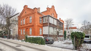 A red brick building with a two-story structure, a gated parking area, and snow on the ground. - Apartamenty Sun & Snow Obrońców Westerplatte 8 (Sopot)