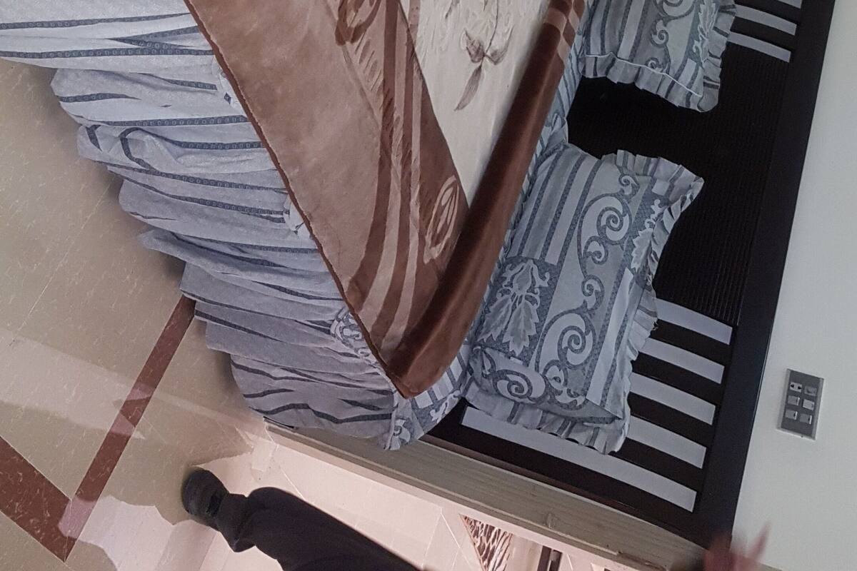 Ein Zimmer mit einem Bett mit gemusterten Bettwäsche, einem Nachttisch mit Lampe und einem an der Wand montierten Telefon.