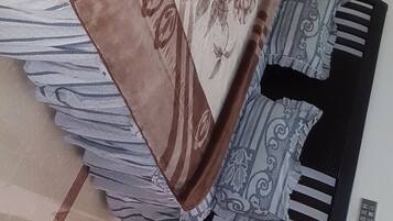 A room with a bed covered in patterned bedding, a bedside table with a lamp, and a wall-mounted telephone.