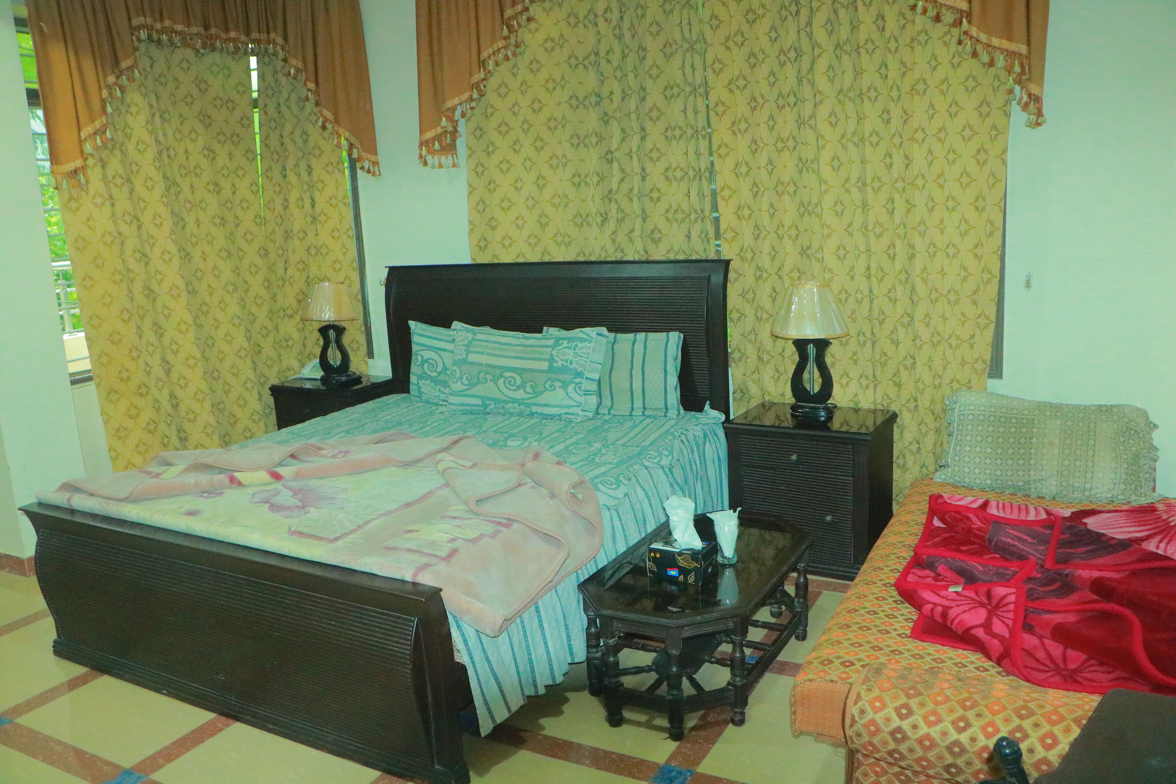 A bedroom with a bed, two bedside tables with lamps, a nightstand, and a sofa.