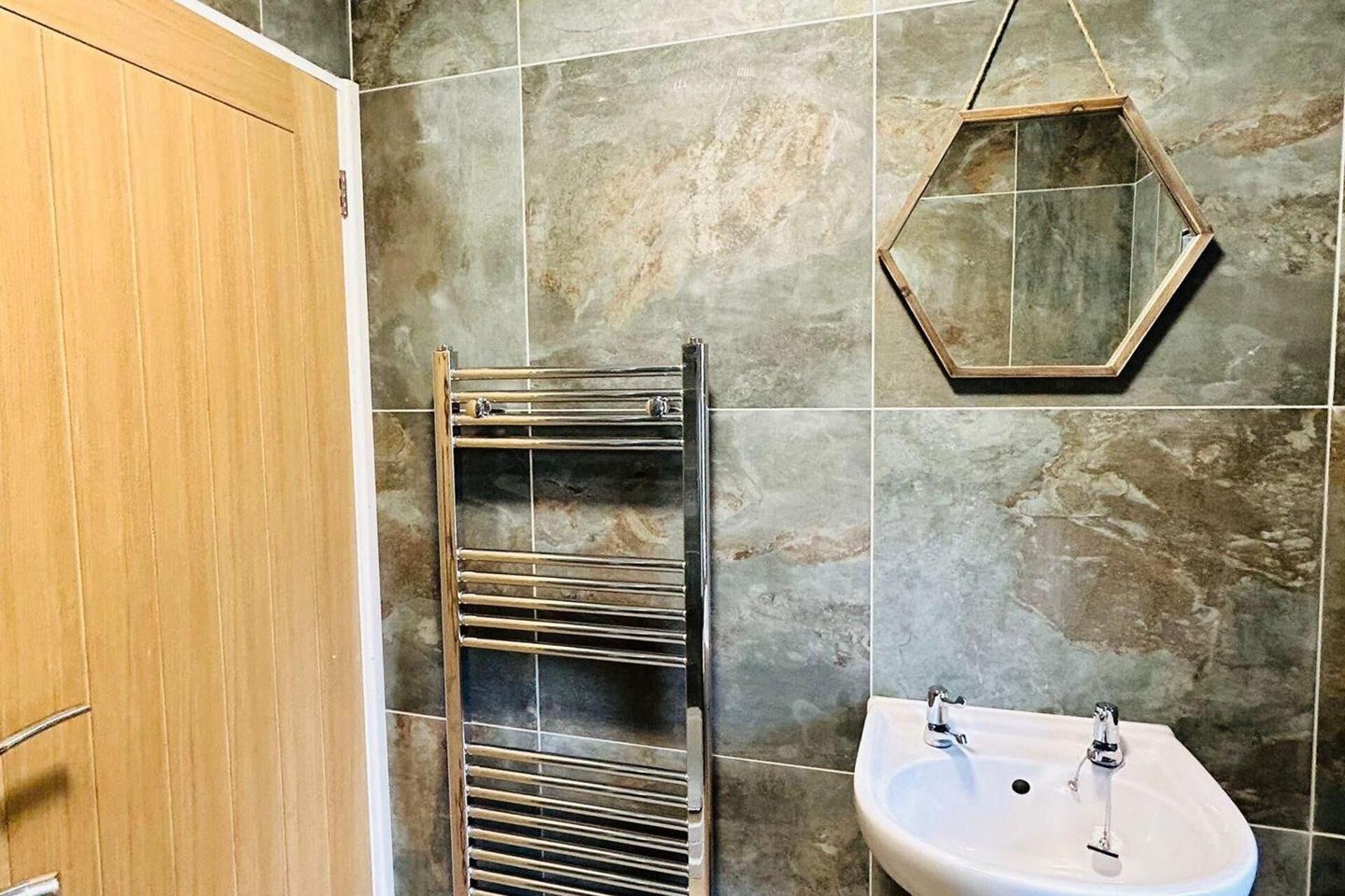 A bathroom with a wooden cabinet, a towel rack, a hexagonal mirror, and a sink.