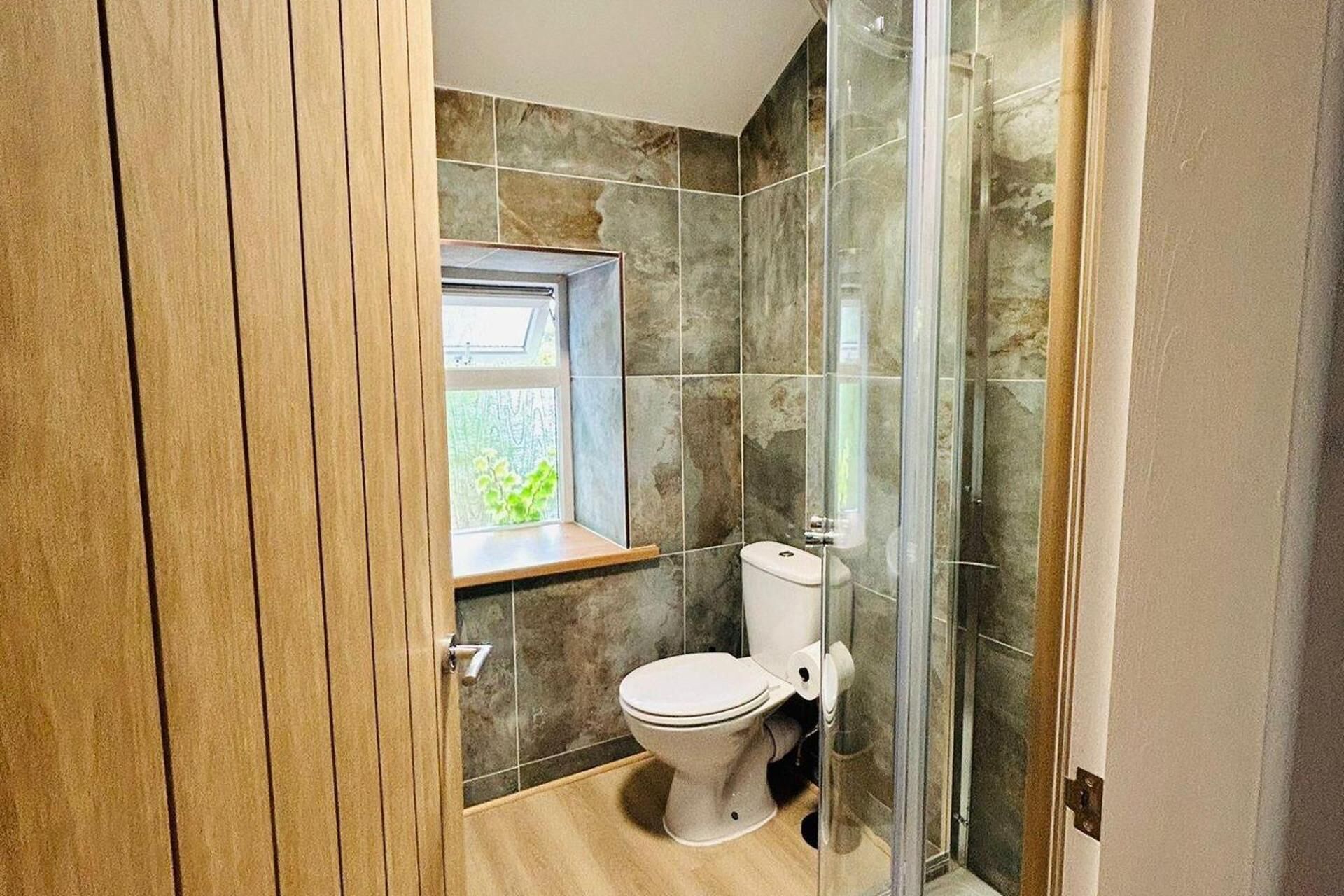 A bathroom with a toilet, a window, and a shower area.