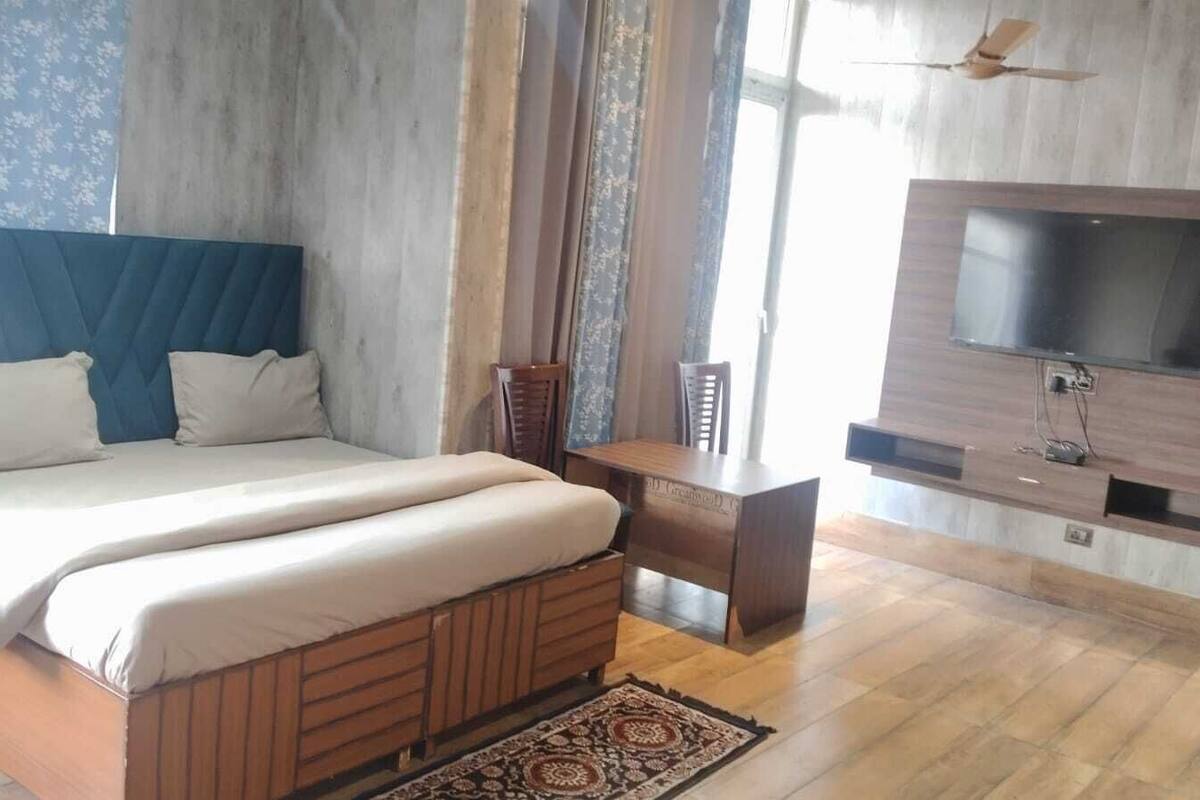 A bedroom with a bed, a desk, a TV mounted on the wall, and a patterned rug.