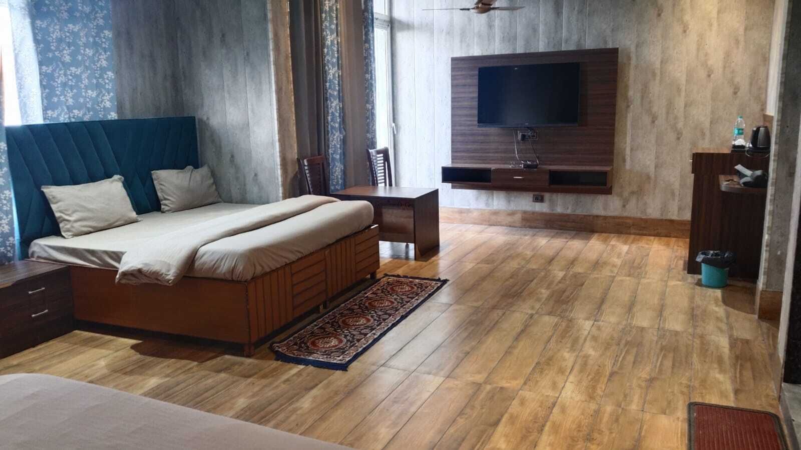 Makuuhuoneessa on sänky, seinälle asennettu televisio, puulattia ja pieni pöytä tuolilla.