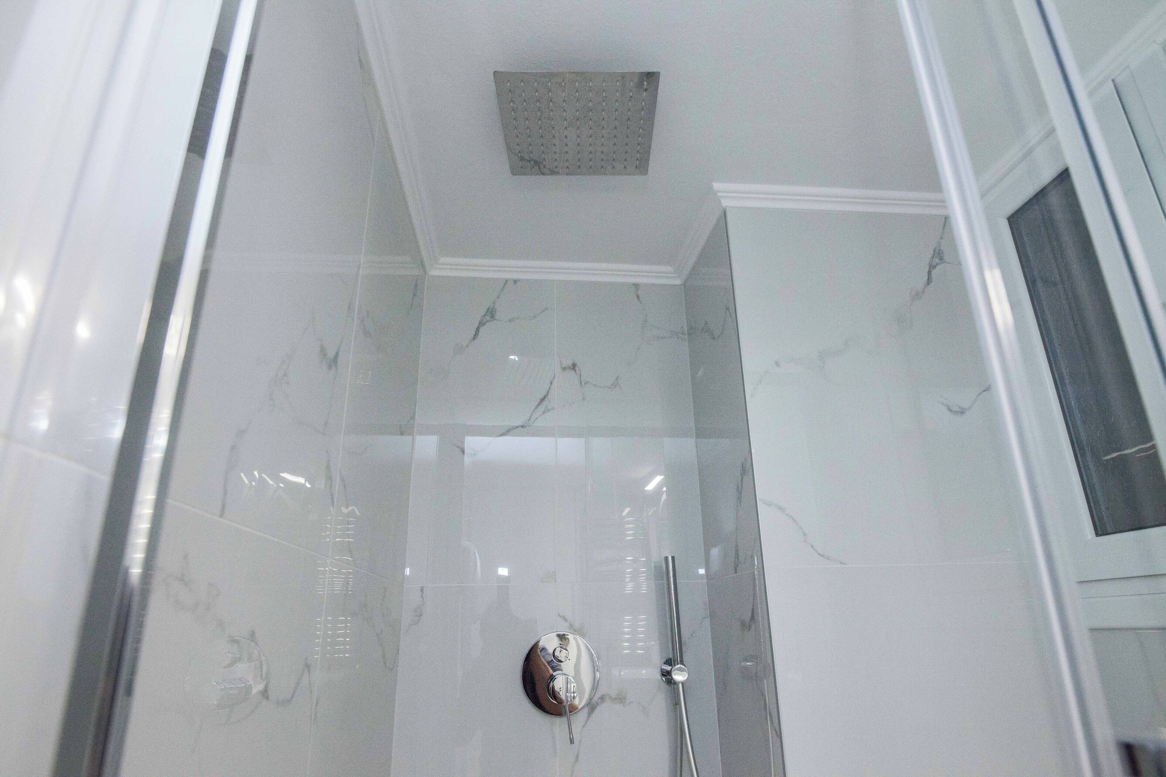 Et moderne badeværelse med glasbrusekabine, marmorfliser og brusehoved monteret i loftet.