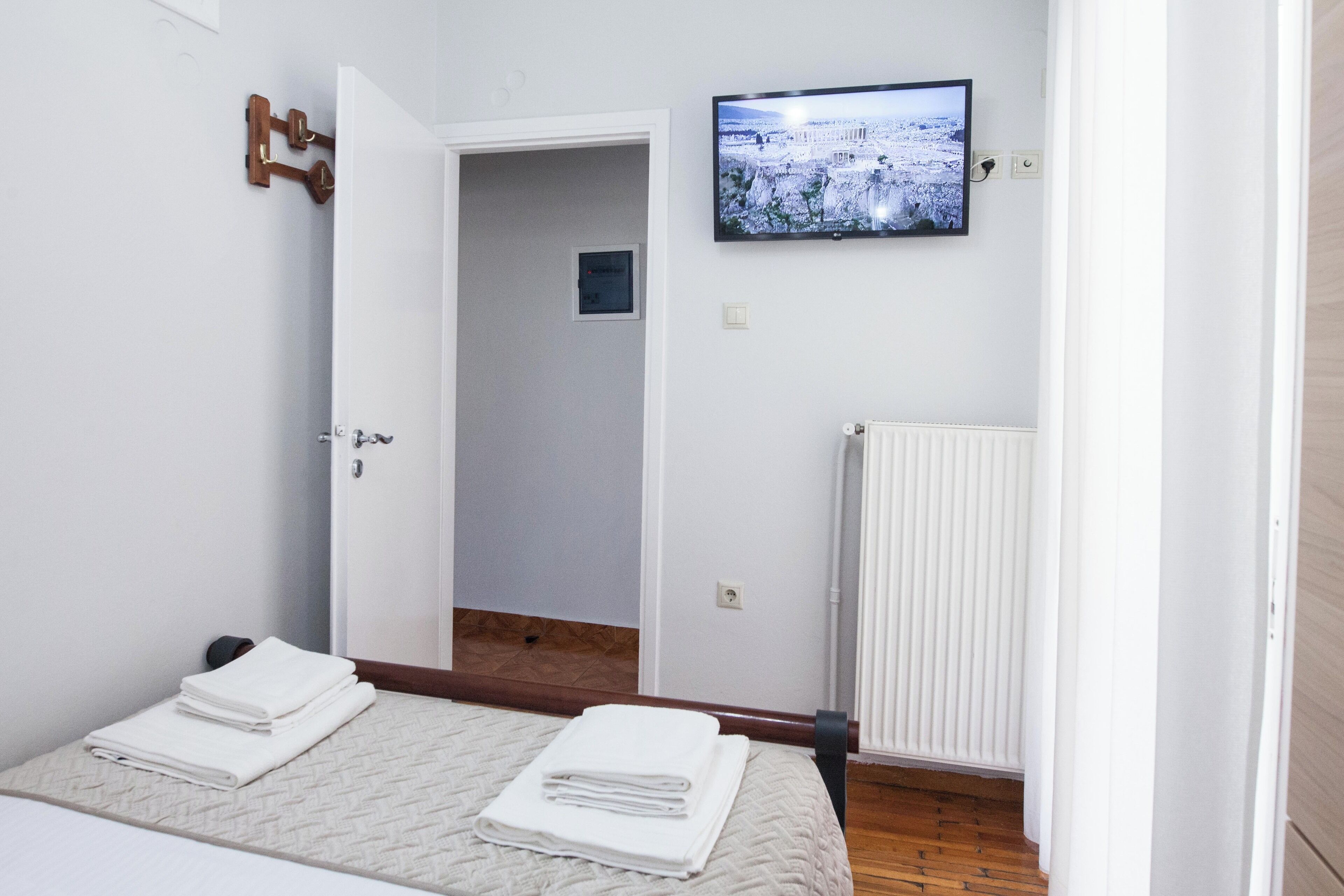 A bedroom with a bed, a TV on the wall, and a door leading to another room.