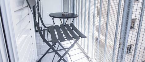 A balcony with a metal table and chairs, a white door, and a metal fence.