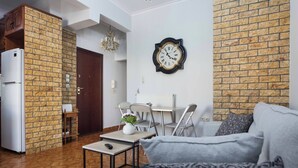 Un salon comprenant un canapé, une table basse et un coin repas avec des chaises et une table. On peut apercevoir un réfrigérateur dans un coin.
