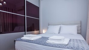 Un lit bien fait, avec une literie blanche et grise, une fenêtre avec des rideaux et un climatiseur fixé au mur.