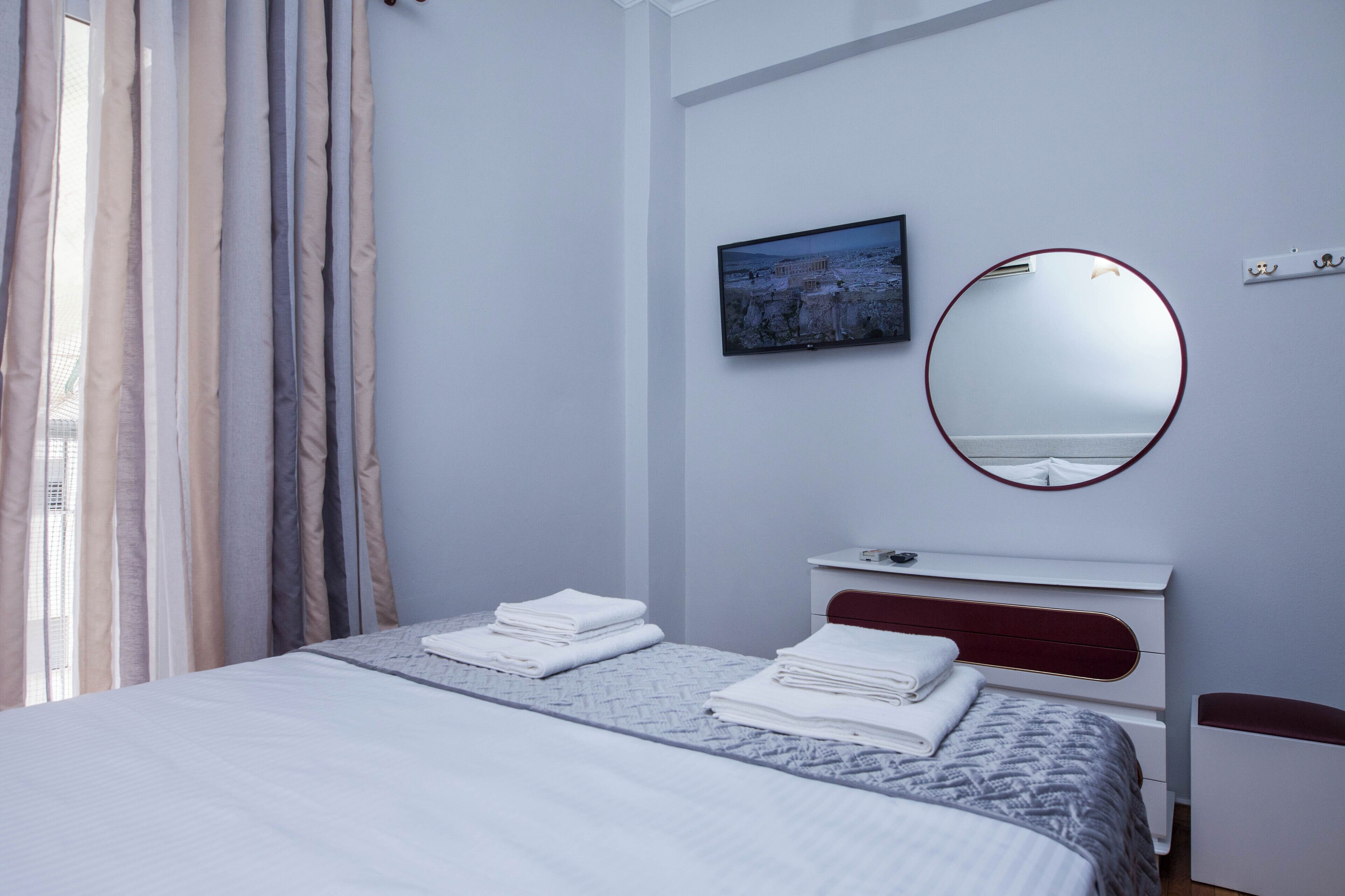 Une chambre à coucher moderne avec un lit, une table de chevet, un miroir et un téléviseur fixé au mur.