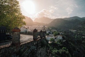Bjergrigt landskab med en stenvæg og en vej, der fører til en by.