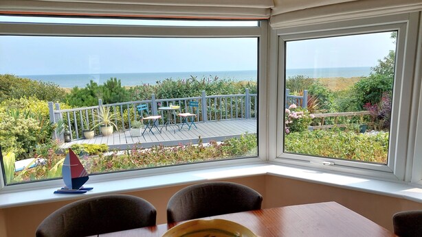 Un comedor con vistas al mar, un balcón con mobiliario exterior y una mesa con un cuenco de fruta.