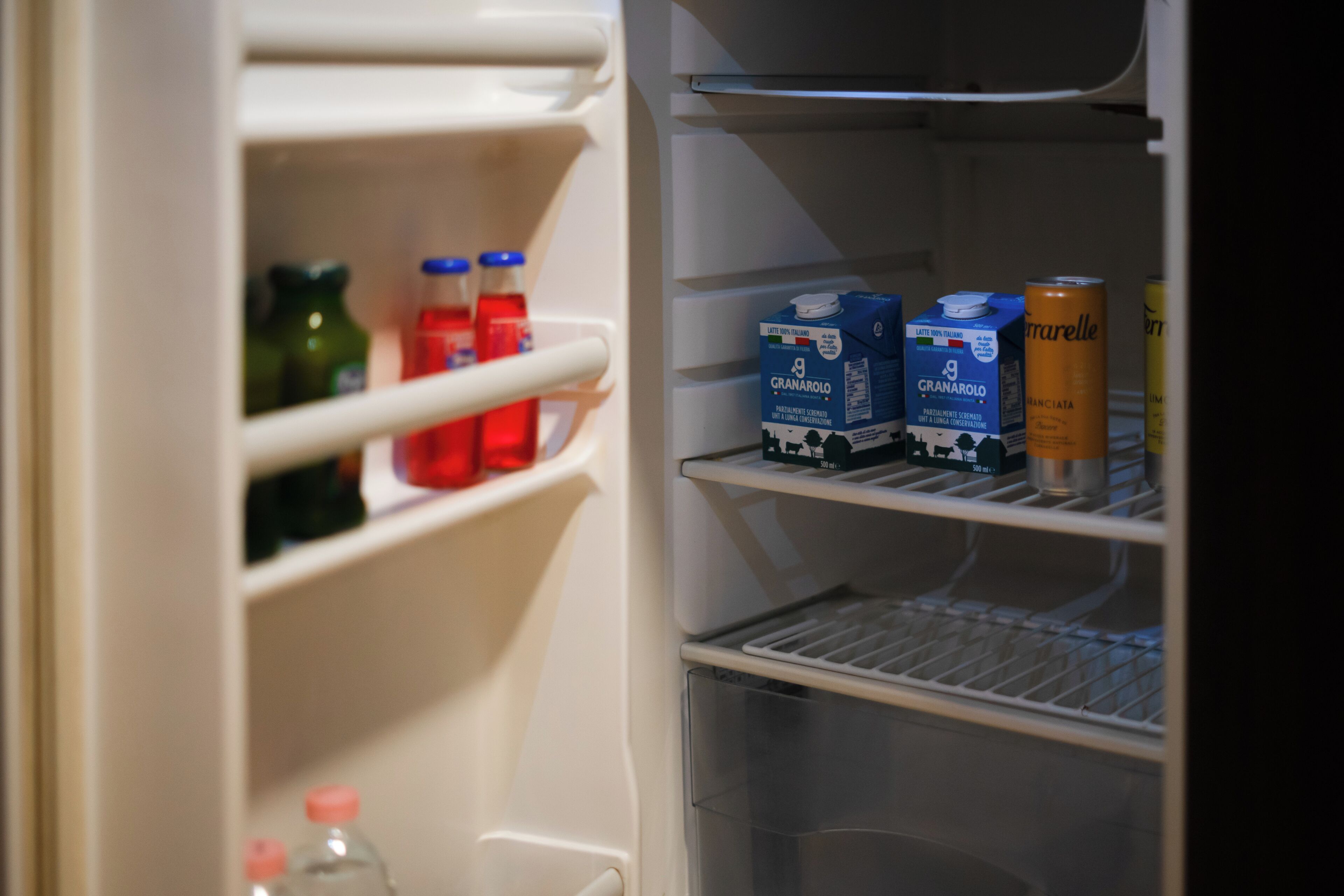 An open refrigerator with shelves containing milk cartons, juice bottles, and a can.