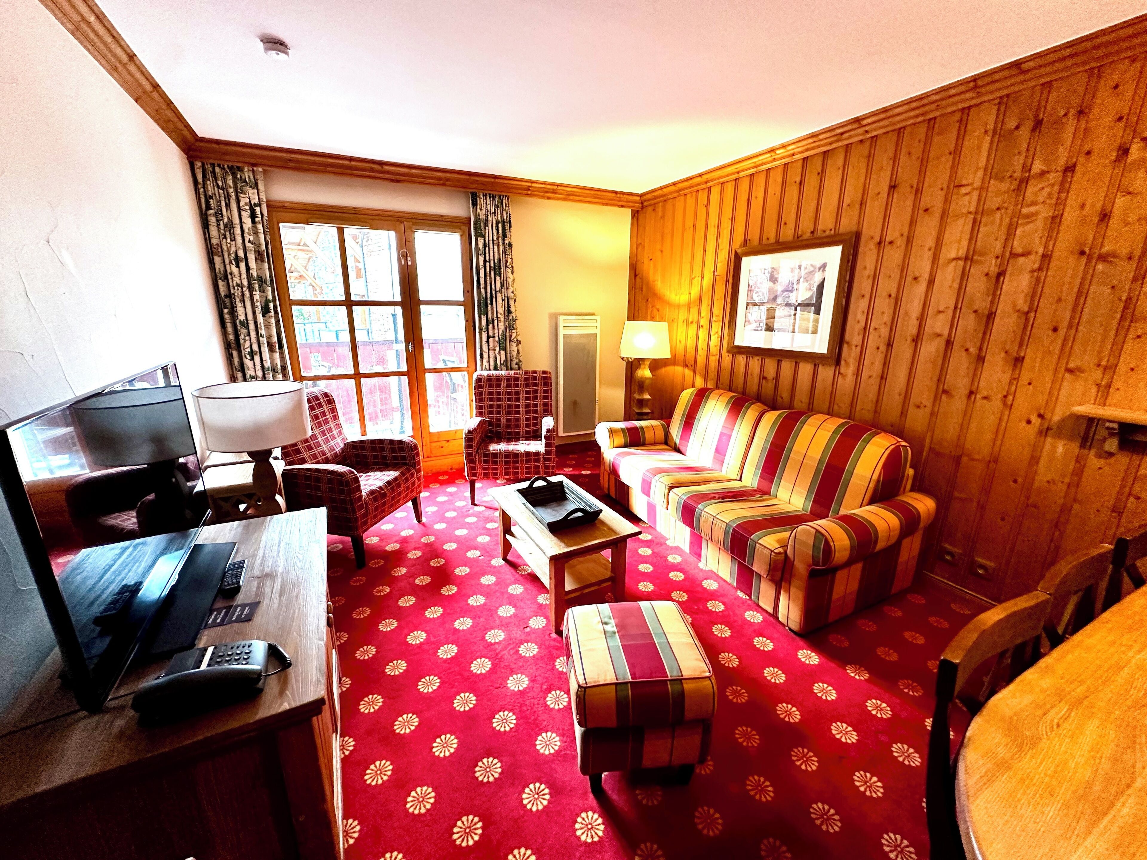 A living room with a red patterned carpet, wooden walls, a sofa, a chair, a coffee table, and a television.