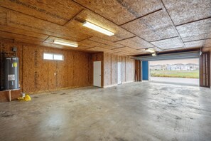 A spacious indoor area with wooden walls and a concrete floor, featuring a large water heater and a window. - Luxury Waterfront Townhome | Pool, Boat Slip & Sunset Views (Corpus Christi)