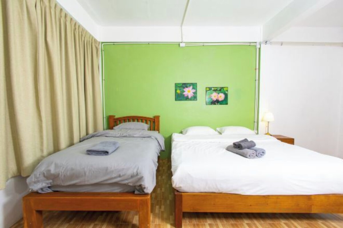 Ein Zimmer mit zwei Holzbetten, einer grünen Wand und einem Fenster mit Vorhängen.