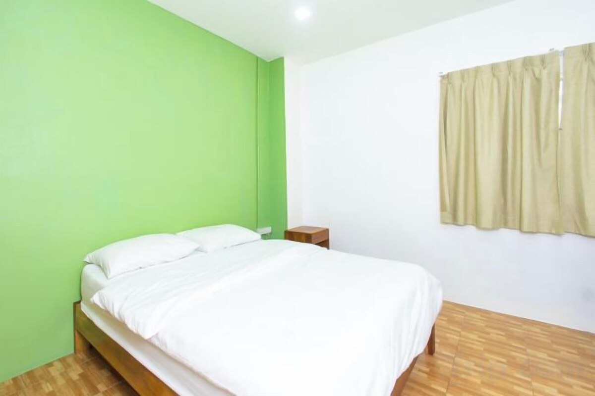 A room with a bed, a nightstand, a window with curtains, and a green wall.