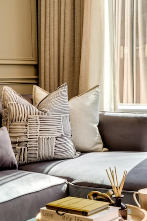 A cozy living room with a grey sofa, patterned cushions, a stack of books, and a decorative tray with reed sticks.
