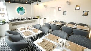 A restaurant with multiple tables set for dining, a kitchen area, and a wall with a globe and framed pictures. - One Earth Elegant Amritsar (Amritsar)