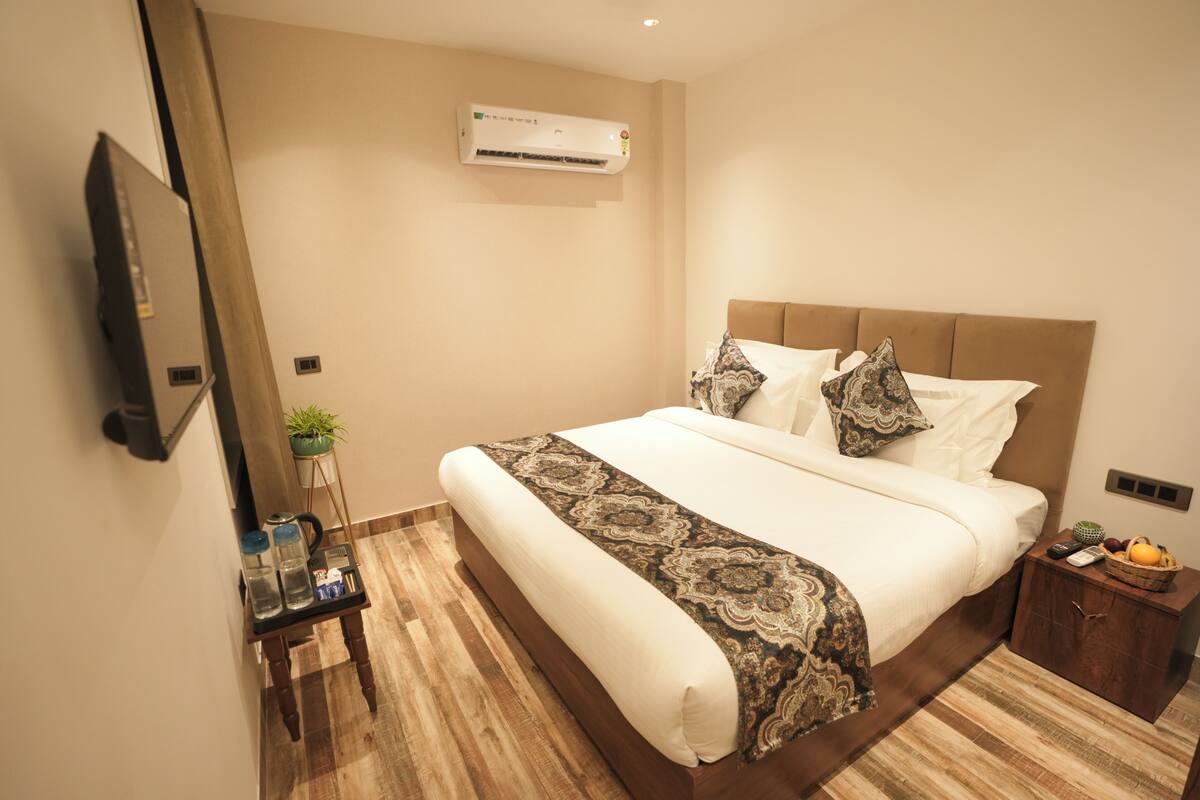 Camera d'albergo con un letto grande, un comodino con una pianta, un piccolo armadietto e un condizionatore d'aria a parete.