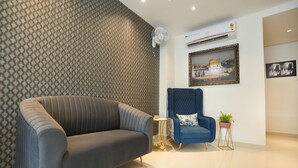 A modern living room with a grey sofa, a blue armchair, and a small round table with a plant. - One Earth Elegant Amritsar (Amritsar)