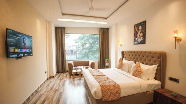 A hotel room with a large bed, a TV on the wall, a window with curtains, and a ceiling fan. - One Earth Elegant Amritsar (Amritsar)
