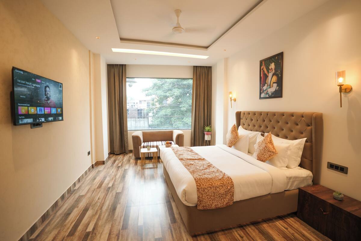Una camera d'albergo con un letto grande, una TV a parete, una finestra con tende e una ventola a soffitto.