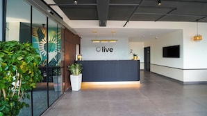 A reception desk with a 'live' sign, a modern interior with a flat ceiling, and a large screen on the wall. - Olive Hotel Benz Circle, Vijayawada by Embassy Group (Vijayawada)